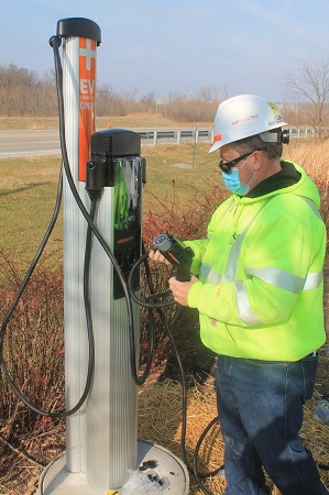 Man in hard hat next to electric vehicle charging station